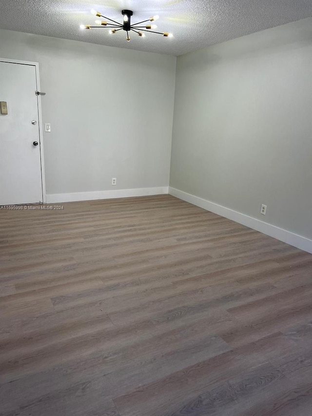 401 Golden Isles Dr Unit 303, Hallandale Beach, FL 33009 - unfurnished room featuring a chandelier, wood finished floors, baseboards, and a textured ceiling