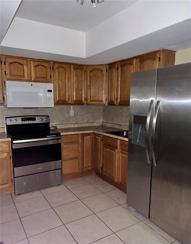 kitchen featuring appliances with stainless steel finishes, light tile patterned flooring, and decorative backsplash