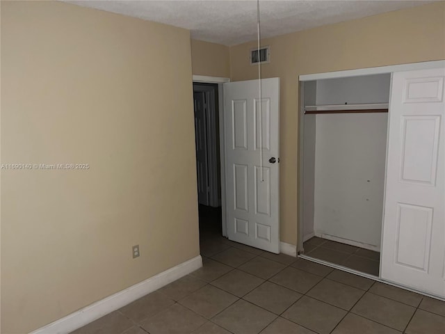 unfurnished bedroom with tile patterned flooring, a textured ceiling, and a closet