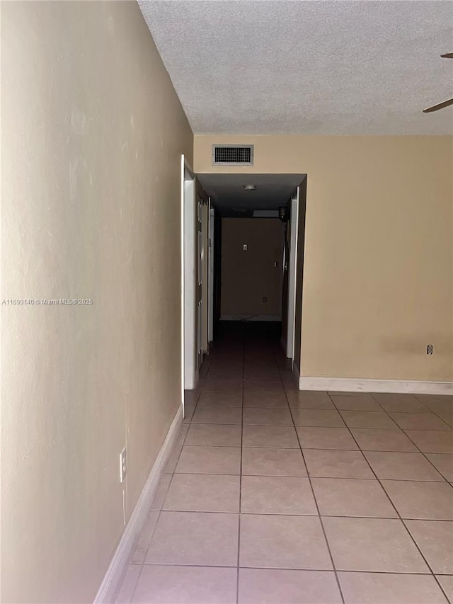 hall with a textured ceiling and light tile patterned floors