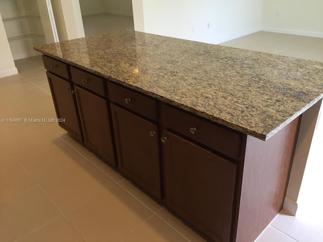 kitchen with dark brown cabinets, a center island, stone countertops, and light tile patterned floors