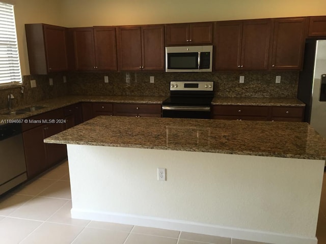 kitchen with dark brown cabinetry, sink, tasteful backsplash, dark stone countertops, and appliances with stainless steel finishes