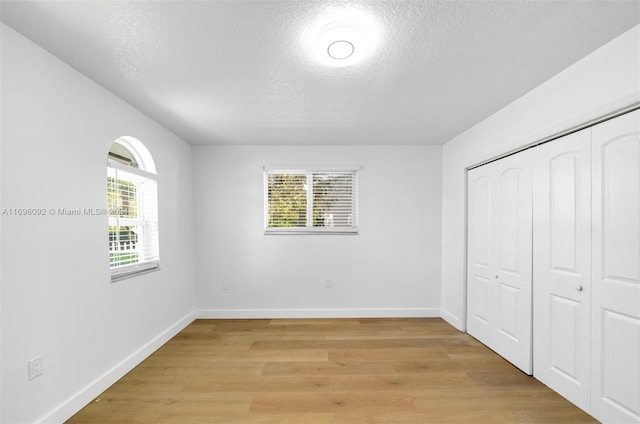 unfurnished bedroom with a textured ceiling, a closet, light hardwood / wood-style flooring, and multiple windows