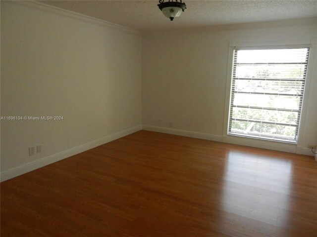 unfurnished room with wood-type flooring, a textured ceiling, and ornamental molding