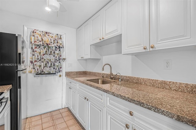 kitchen featuring dark stone counters, sink, ceiling fan, white cabinetry, and stainless steel refrigerator