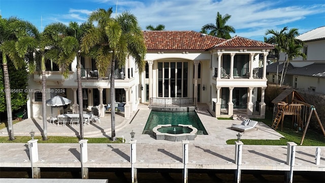 back of house with a balcony, a patio area, and a pool with hot tub