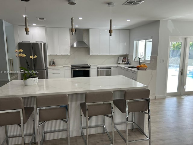 kitchen featuring pendant lighting, wall chimney exhaust hood, sink, and stainless steel appliances