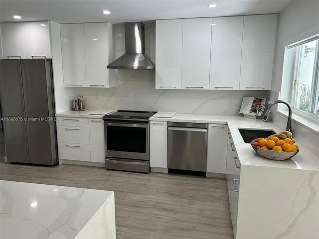 kitchen featuring white cabinetry, sink, stainless steel appliances, and wall chimney range hood