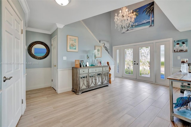 entrance foyer with light wood-type flooring, a wainscoted wall, ornamental molding, french doors, and an inviting chandelier