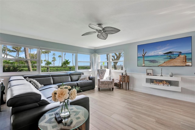 living area featuring a lit fireplace, wood finished floors, wainscoting, and crown molding