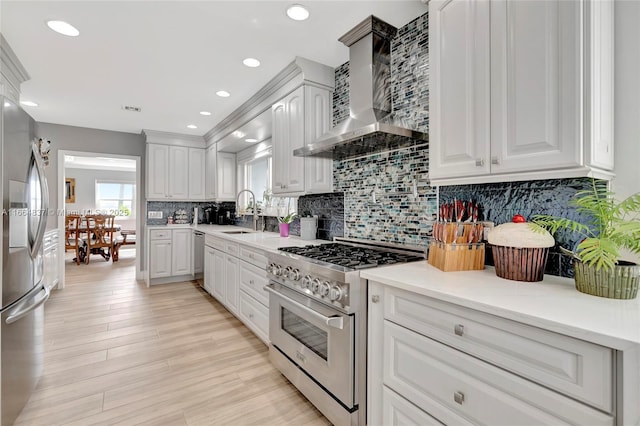 kitchen with wall chimney range hood, decorative backsplash, stainless steel appliances, white cabinetry, and a sink