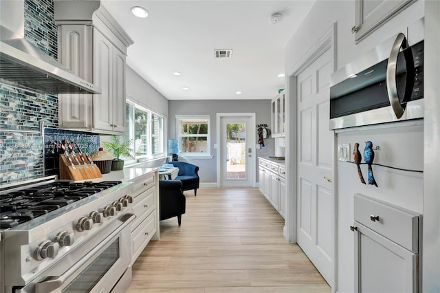 kitchen with visible vents, light wood finished floors, stainless steel appliances, wall chimney range hood, and tasteful backsplash