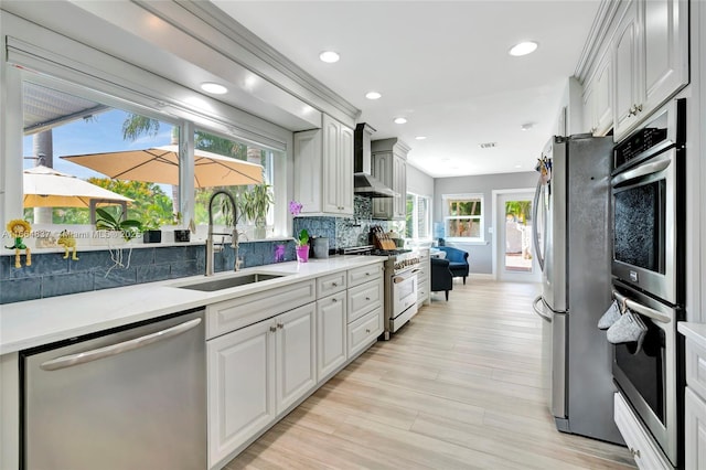 kitchen featuring a sink, decorative backsplash, light countertops, appliances with stainless steel finishes, and wall chimney range hood