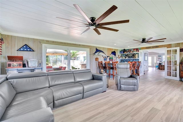 living area featuring wooden walls, wood finished floors, ceiling fan, ornamental molding, and french doors