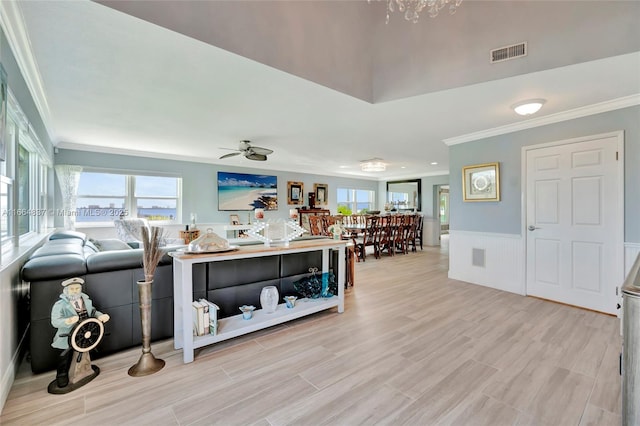 living room featuring a ceiling fan, visible vents, light wood finished floors, ornamental molding, and wainscoting