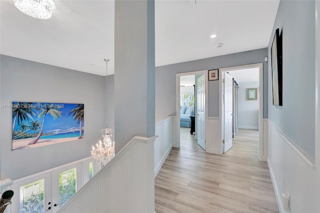 corridor featuring an upstairs landing, light wood-style floors, wainscoting, and a chandelier