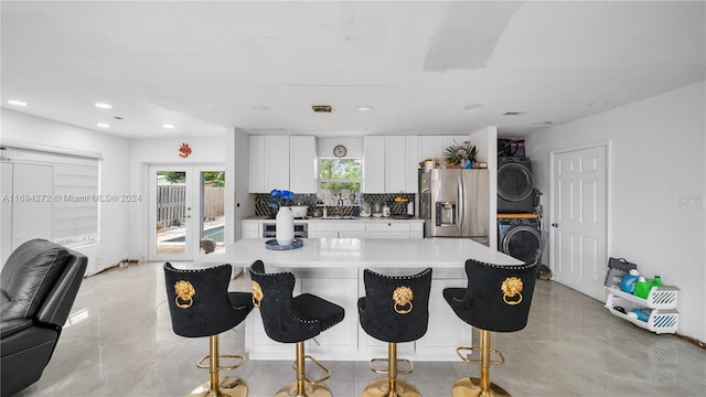 kitchen with french doors, stainless steel refrigerator with ice dispenser, a breakfast bar area, white cabinets, and stacked washer and clothes dryer