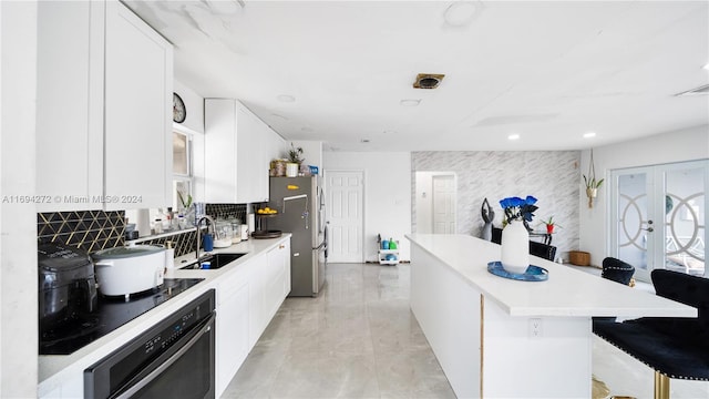 kitchen with a breakfast bar, white cabinets, sink, stainless steel fridge, and black oven