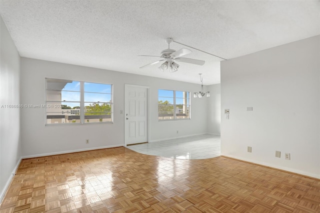 empty room with ceiling fan with notable chandelier, a textured ceiling, and light parquet floors