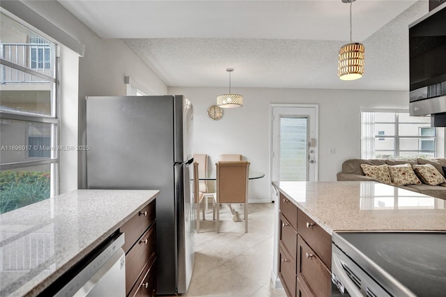 kitchen featuring light tile patterned floors, a textured ceiling, appliances with stainless steel finishes, light stone counters, and hanging light fixtures