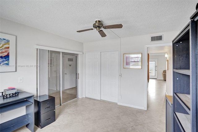 bedroom featuring ceiling fan, light tile patterned floors, a textured ceiling, and multiple closets