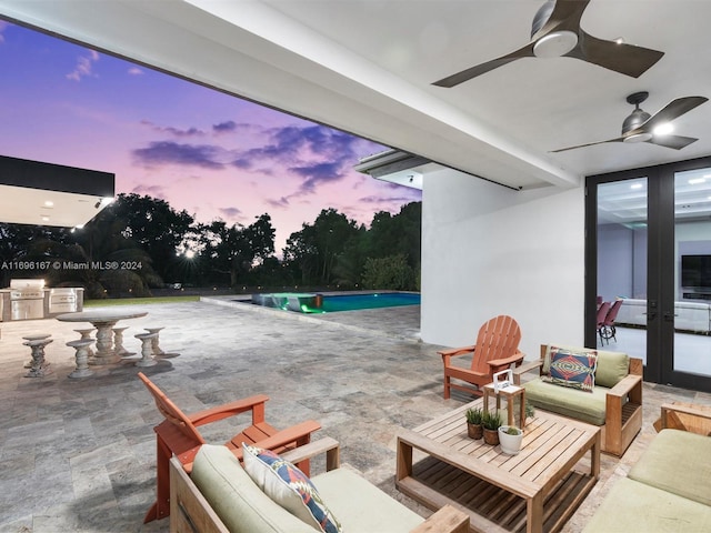 patio terrace at dusk with outdoor lounge area, ceiling fan, an outdoor kitchen, and a grill