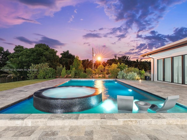 pool at dusk featuring a patio area and an in ground hot tub