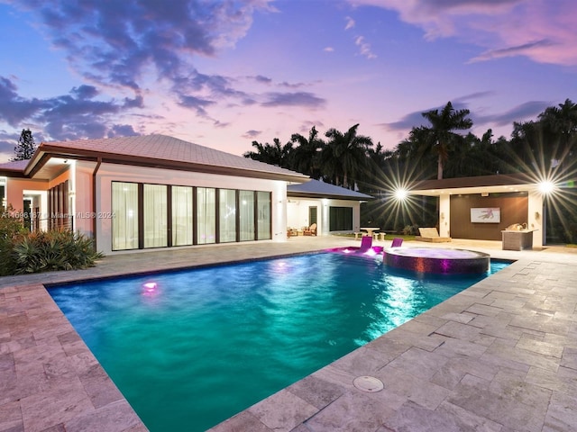 pool at dusk featuring an in ground hot tub and a patio