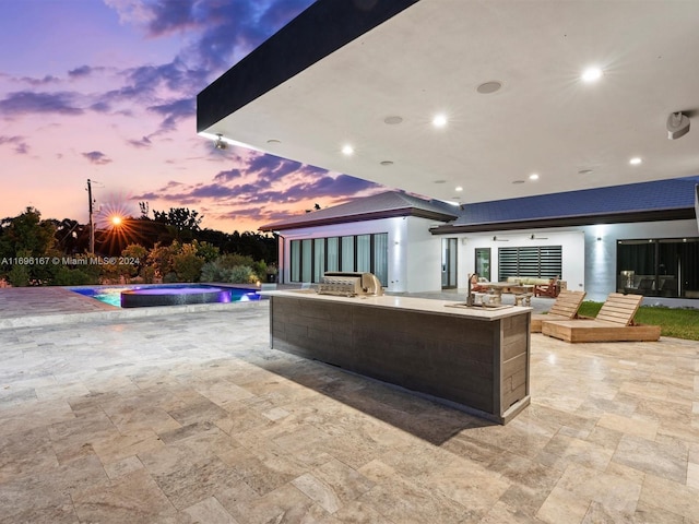 patio terrace at dusk with an outdoor kitchen, a pool with hot tub, and area for grilling