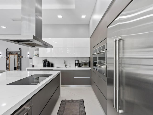 kitchen featuring gray cabinetry, light stone countertops, island range hood, white cabinetry, and stainless steel appliances