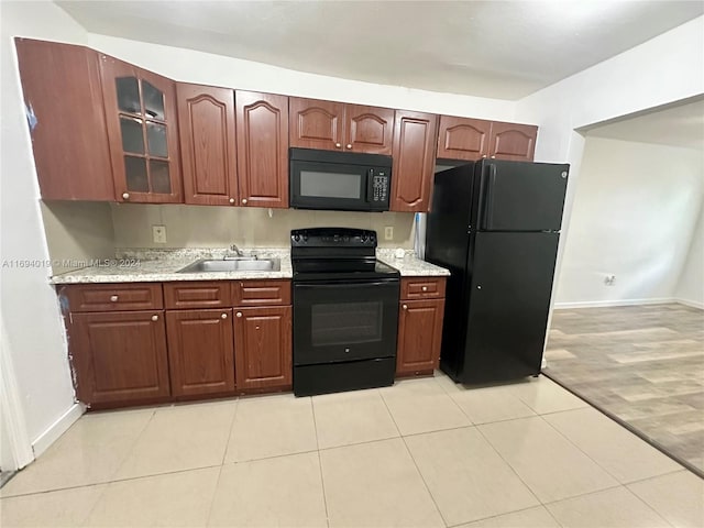 kitchen featuring light stone counters, sink, black appliances, and light wood-type flooring