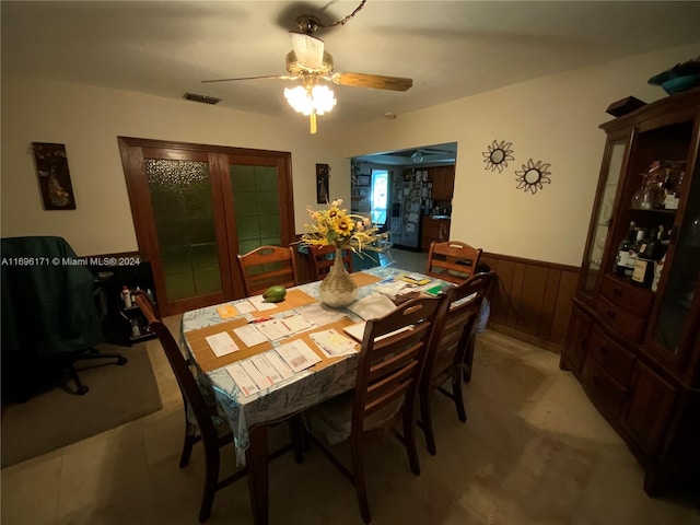 dining space with ceiling fan and wood walls