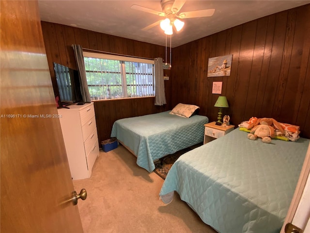 bedroom with ceiling fan, wooden walls, and light carpet