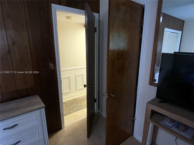 hallway with light colored carpet and wooden walls