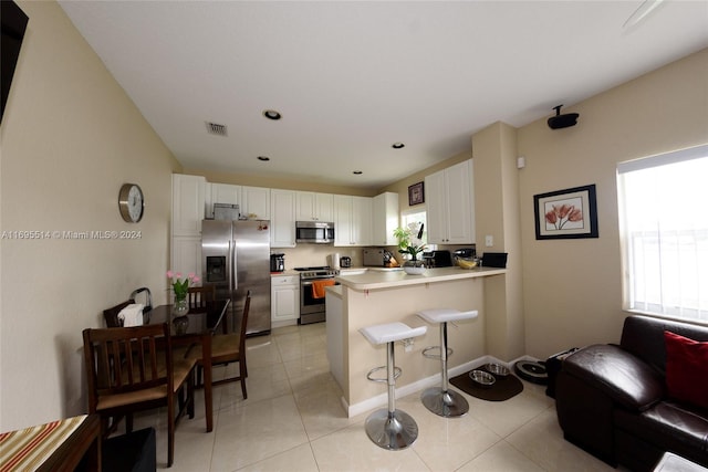 kitchen with a kitchen breakfast bar, white cabinetry, kitchen peninsula, and stainless steel appliances