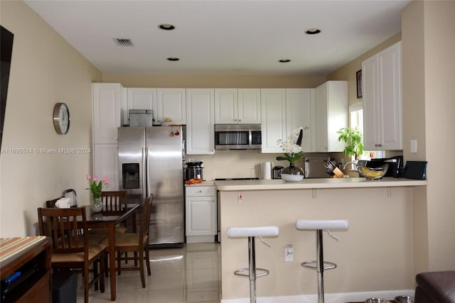 kitchen featuring kitchen peninsula, a kitchen breakfast bar, stainless steel appliances, and white cabinetry