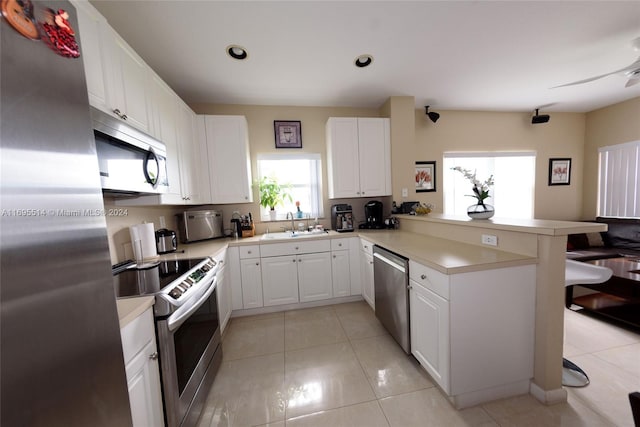 kitchen with kitchen peninsula, appliances with stainless steel finishes, white cabinets, a breakfast bar area, and light tile patterned flooring