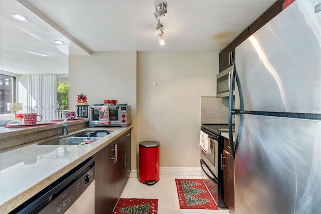 kitchen featuring appliances with stainless steel finishes, rail lighting, light stone counters, sink, and light tile patterned floors