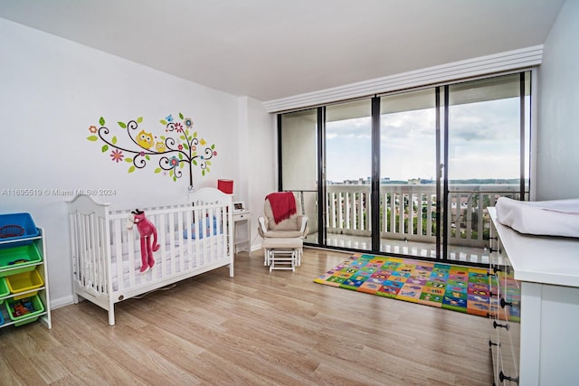 bedroom with floor to ceiling windows, light wood-type flooring, and a nursery area