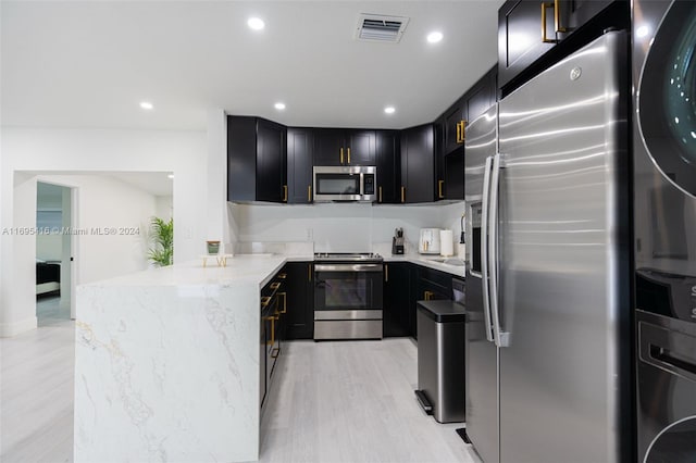 kitchen featuring kitchen peninsula, appliances with stainless steel finishes, light hardwood / wood-style floors, and light stone counters