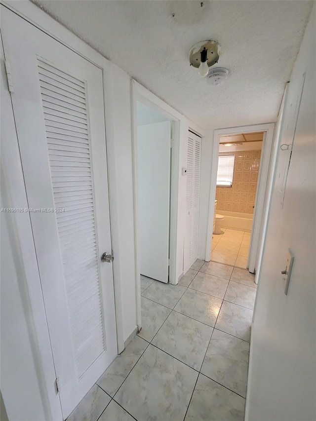 hall featuring light tile patterned floors and a textured ceiling