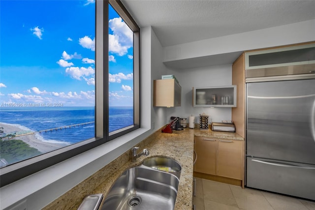 kitchen featuring a textured ceiling, sink, light tile patterned floors, a water view, and stainless steel built in fridge