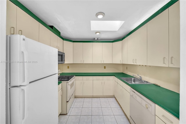 kitchen with white appliances, cream cabinets, sink, a skylight, and light tile patterned flooring