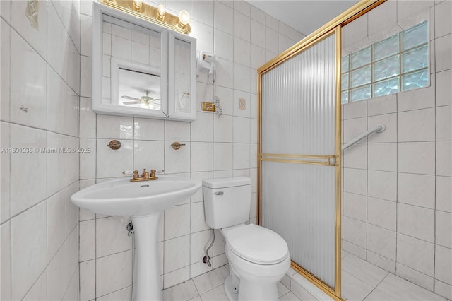 bathroom with a shower with door, sink, ceiling fan, toilet, and tile walls