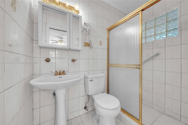 bathroom featuring a shower stall, ceiling fan, toilet, tile walls, and a sink