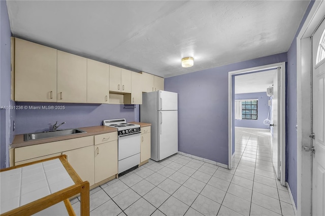 kitchen with cream cabinetry, white appliances, sink, and light tile patterned floors