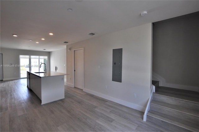 kitchen featuring electric panel, a center island with sink, light hardwood / wood-style floors, and sink