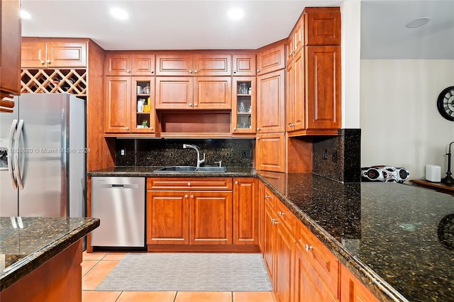 kitchen with backsplash, stainless steel appliances, sink, light tile patterned floors, and dark stone countertops