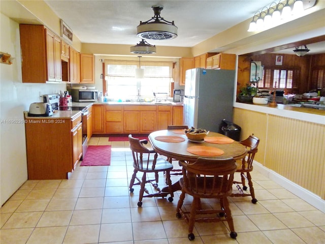 kitchen featuring sink, wood walls, decorative light fixtures, light tile patterned flooring, and appliances with stainless steel finishes