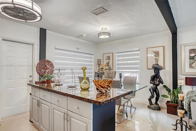 kitchen featuring a center island, light tile patterned floors, white cabinetry, and dark stone counters